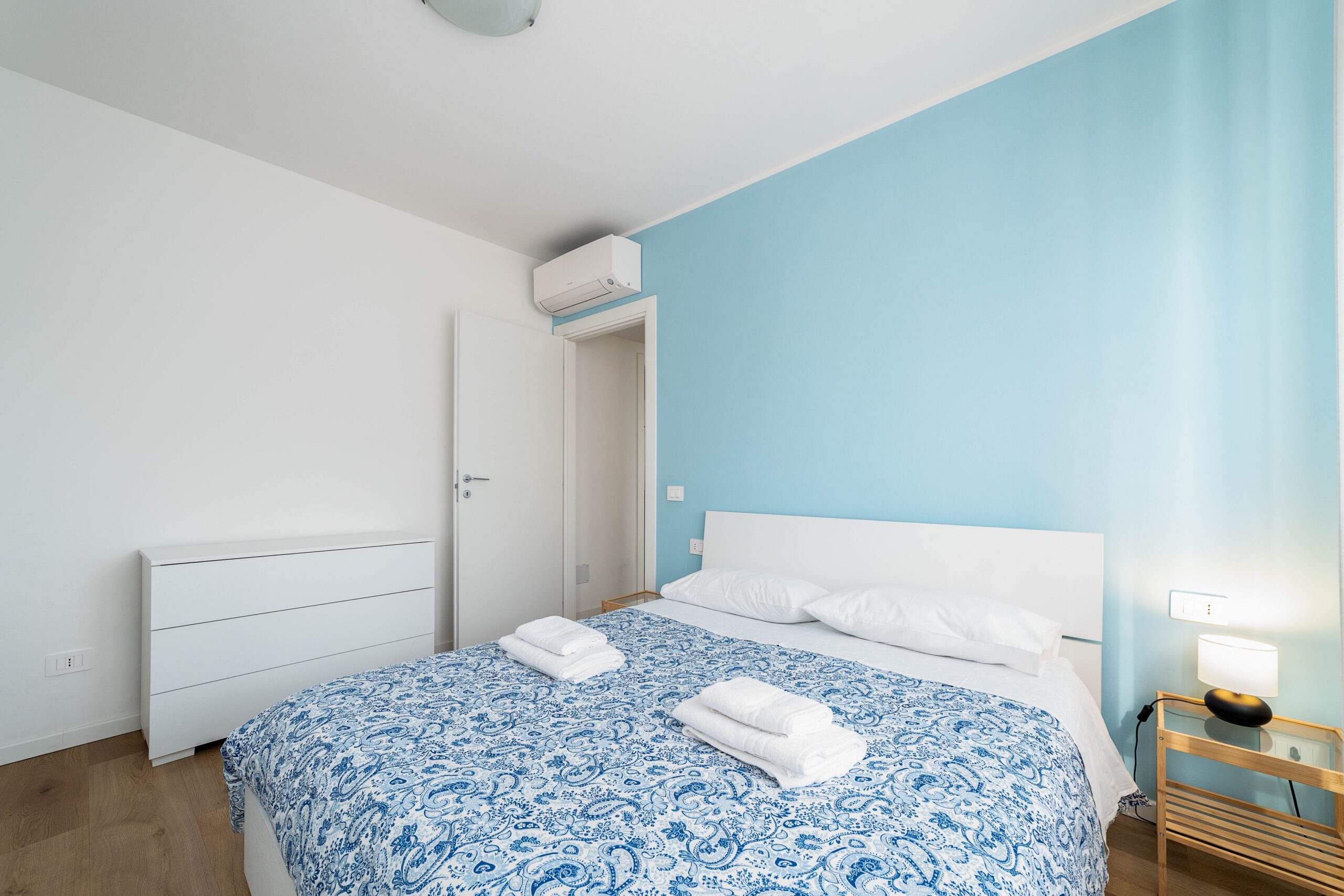 Camera matrimoniale con parete azzurra aria condizionata e comodini appartamento vacanze Monza