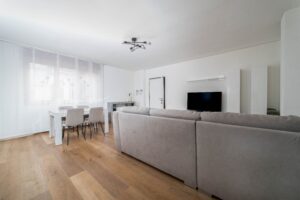 Soggiorno con divano grigio tavolo pranzo e TV parquet appartamento vacanze BNB Monza