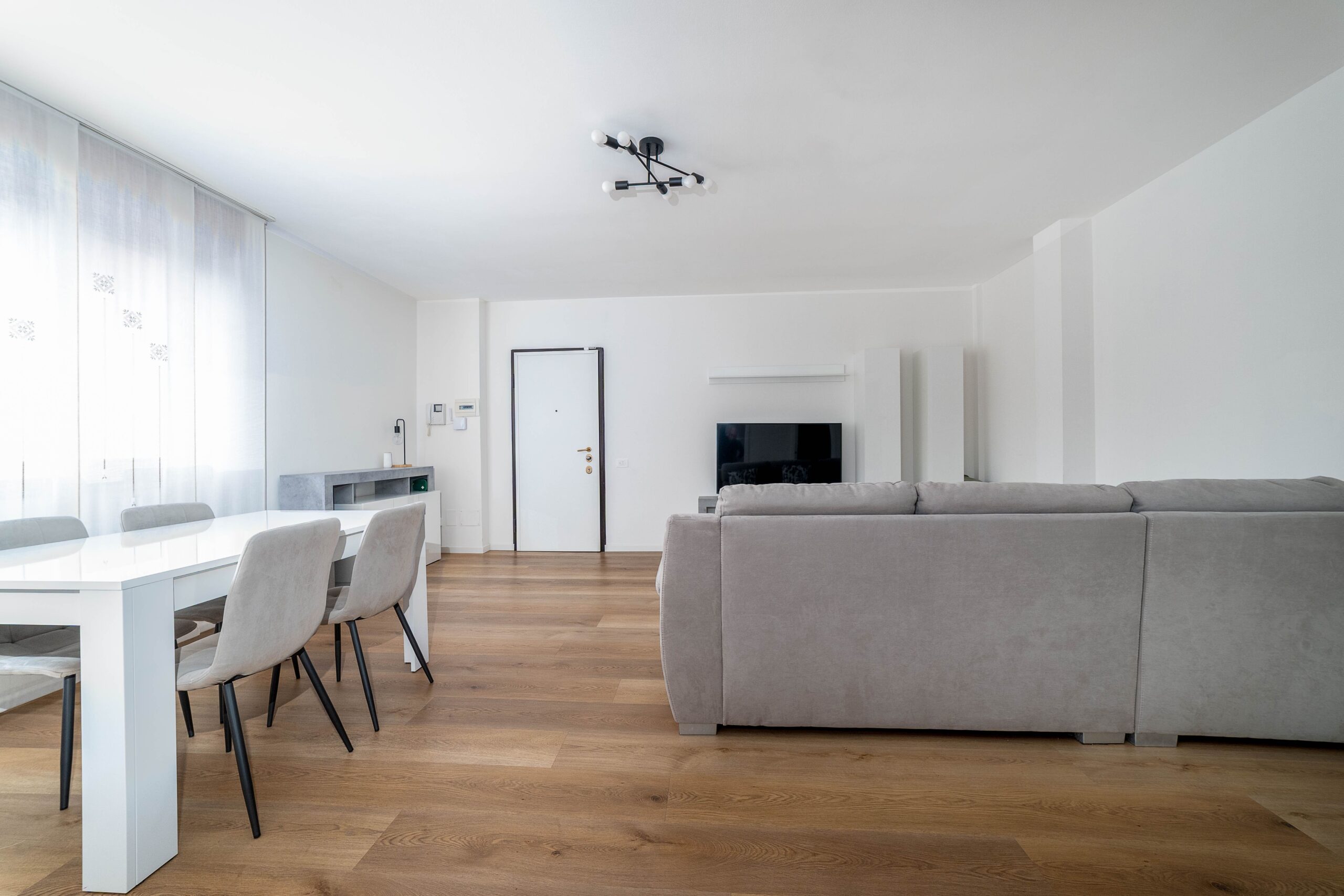 Soggiorno con divano grigio tavolo pranzo e TV parquet appartamento vacanze